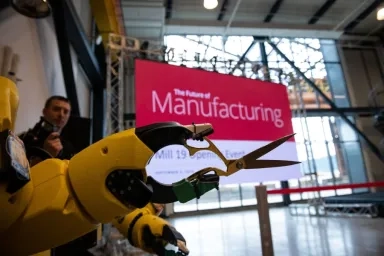 A robotic arm holding scissors at a manufacturing event on CMU's campus with a large "The Future of Manufacturing" sign in the background